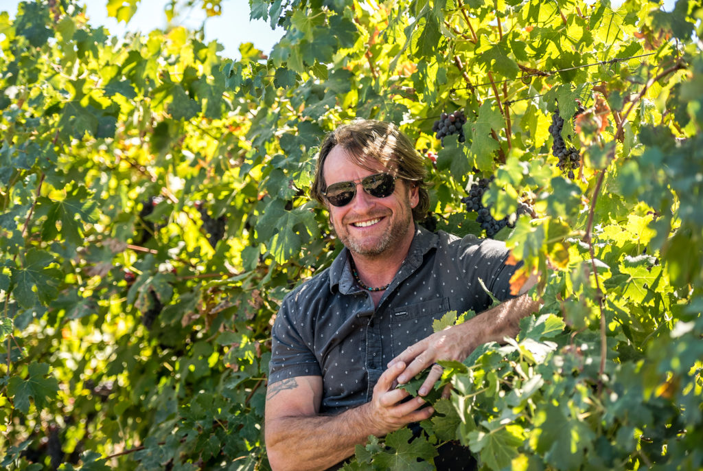 Adam LaZarre smiling amid grape vines