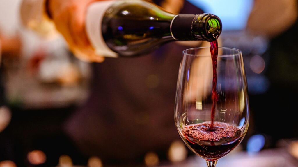 A server pours red wine into a wine glass.