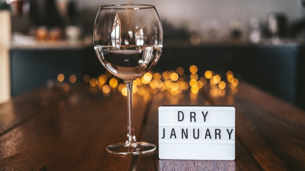 A wine glass filled with water next to a sign that says “Dry January”.