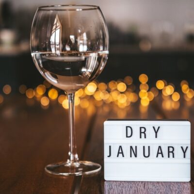 A wine glass filled with water next to a sign that says “Dry January”.